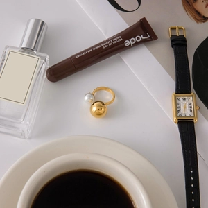 Flatlay of gold open ring with pearl and sphere on a white desk with fashion accessories