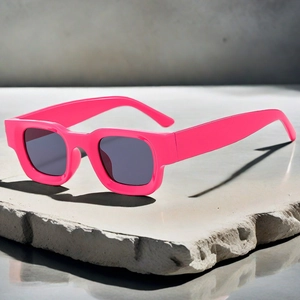 Detail shot of bright rose red rectangular sunglasses on a textured grey stone pedestal