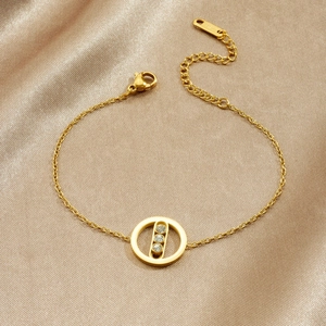 Minimalist gold plated stainless steel bracelet with three clear zircons on satin background