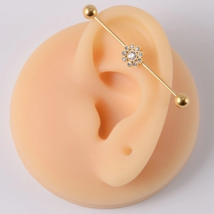 Detail of gold industrial barbell with crystal flower on silicone ear model