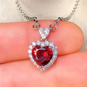 Detailed macro view of heart-shaped silver necklace with a red gemstone and zircon accents