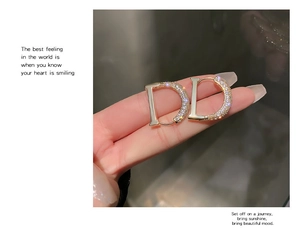 Detail view of gold letter D earrings with white zircon pavé and secure buckle closure
