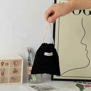 Detail of hand holding black corduroy drawstring pouch with white woven brand label