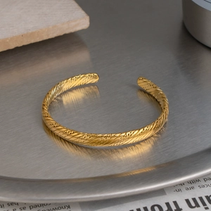 Close-up of golden woven C-shaped open bangle with intricate retro textured detail