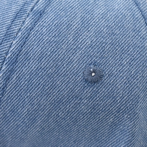 Macro detail of washed denim baseball cap featuring an embroidered eyelet and twill texture