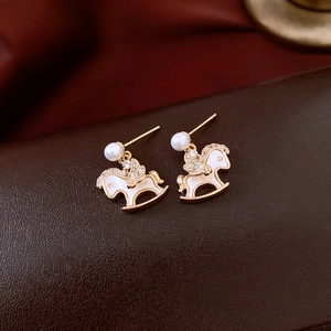 Détail de boucles d'oreilles poney plaquées or 14k avec émail blanc, perles et zircons