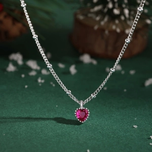 Macro detail of a heart-shaped ruby pendant on a silver chain with festive background