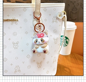 Detail shot of a cute panda keychain with a glowing heart pendant hanging on a white handbag