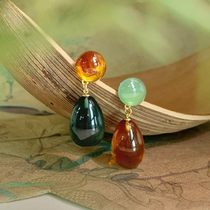 Asymmetric resin teardrop earrings in amber and green with gold accents on wood stand