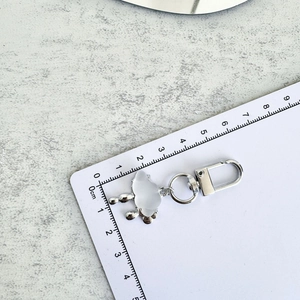Detail view of a silver cloud keychain showing precise dimensions on a metric ruler