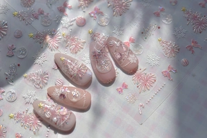 Macro detail of Christmas nail stickers with snowflakes and festive trees on pink nails