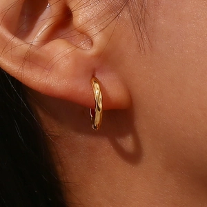 Close-up of gold hoop earring with irregular lava texture worn on ear lobe