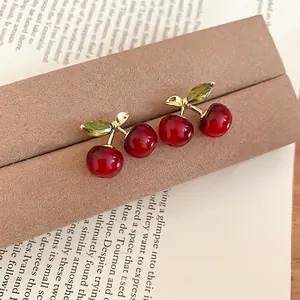 Elegant red resin cherry earrings with green zircon leaves on a vintage book background