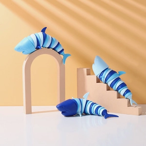 Three 3D-printed flexible shark fidget toys in gradient blue on a warm studio backdrop