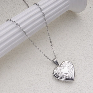 Detail of silver heart locket necklace with floral engraving on a white Roman column