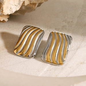 Macro detail of two-tone gold and silver wave pattern rectangular earrings on stone