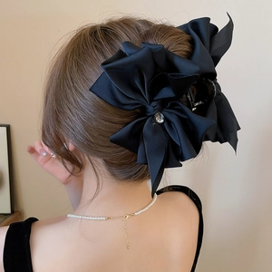 Large black fabric bow hair claw clip with crystal rhinestone center shown on hair