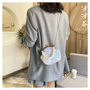 Mini sequin shell bag with large pearl handle and chain strap shown in a cafe setting