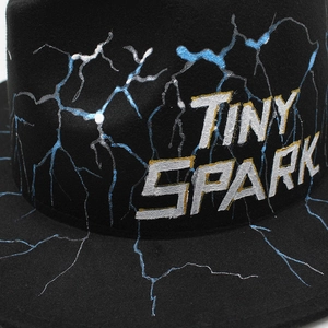 Detail of Tiny Spark branding and blue lightning print on black wool felt fedora hat