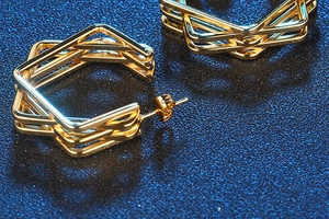 Detail shot of golden multi-layer hexagonal earrings on a shimmering blue surface