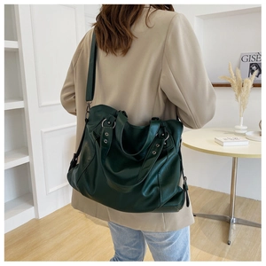 Dark green leather tote bag worn by a model in a minimalist modern interior setting