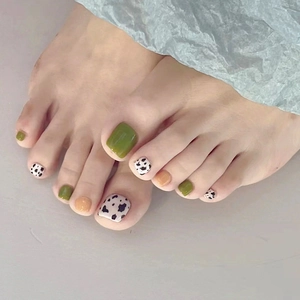 Close-up of green and nude press-on toenails with black and white cow print designs
