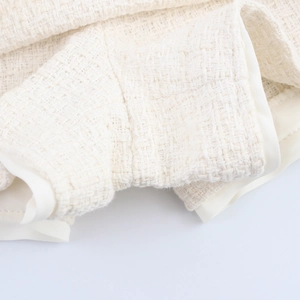 Close-up of white tweed fabric texture with detailed piping craftsmanship on the garment