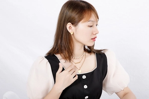 Detail of layered gold necklace set with pearl, heart, and bar charms on model