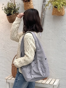 Large gray-blue plaid tote bag with front pockets shown in a scenic outdoor setting