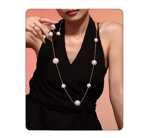 Vue détaillée d'un long collier doré orné de grandes perles blanches sur vêtement noir