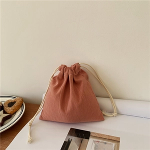 Minimalist cotton linen drawstring storage bag in coral orange on a white magazine