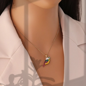 Close-up of golden necklace featuring a vibrant enamel bird pendant worn by a model