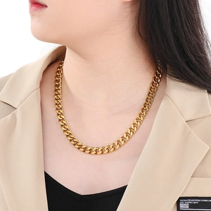 Close-up of a bold gold Cuban link chain necklace worn on a model in a beige blazer