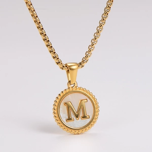 Macro shot of gold pendant with white shell inlay and letter M detail on box chain