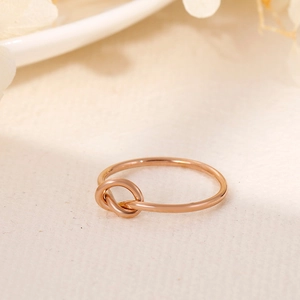 Close-up of rose gold stainless steel knot ring on a minimalist textured surface