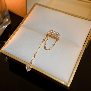 Detail of gold double ear cuff with heart zircon pendant and pearls on beige jewelry box