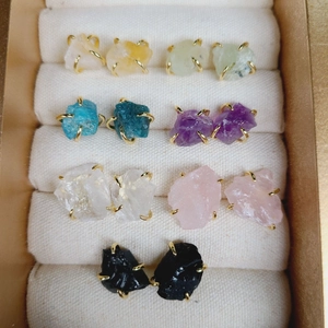 Close-up of seven pairs of natural stone stud earrings with golden 4-claw settings