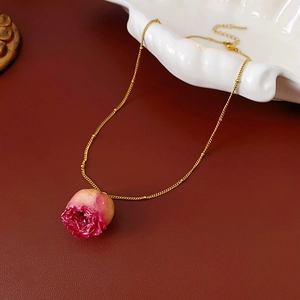 Detail of pink dried rose pendant with golden stem and fine chain on red leather background