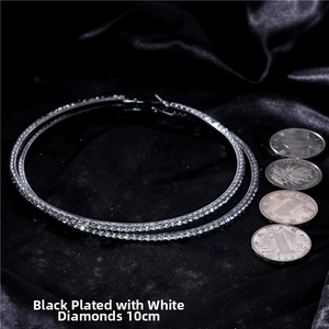 Close-up of gunmetal large hoop earrings encrusted with white crystals next to a coin