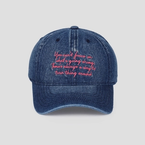 Gros plan sur une casquette en jean bleu délavé avec broderie cursive rose