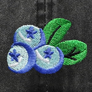 Vue macro détaillée de l'écusson brodé de myrtilles sur une casquette en jean noir
