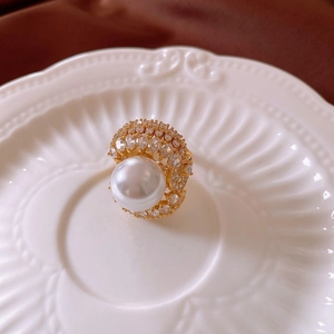 Détail d'une bague dorée avec grande perle et zircons sur un plateau en céramique blanc