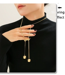 Detail of adjustable golden tassel necklace with hollow ball pendant on black clothing