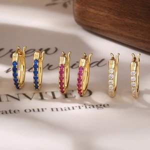 Detail shot of three gold hoop earrings with blue, rose red, and white cubic zirconia
