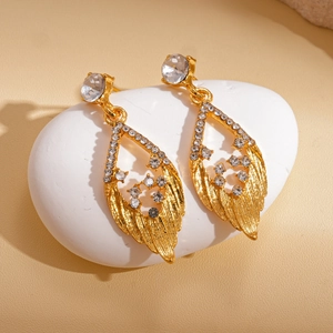 Golden leaf earrings with clear rhinestones on a white pebble in warm lighting
