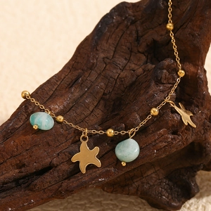 Detail of 18K gold star starfish pendant anklet with turquoise stones on rustic wood
