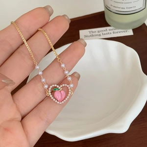 Dettaglio di un ciondolo a cuore con pesca e perle su una collana a catena dorata