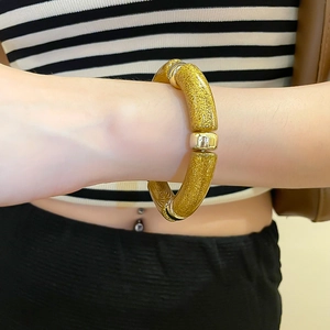 Detail of chunky golden glitter acrylic geometric bangle with metallic spacers on wrist