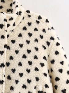 Close-up of thick white fleece jacket featuring high-quality black heart print pattern