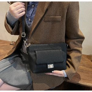 Détail du sac bandoulière noir plissé avec fermoir rotatif doré sur un banc en bois